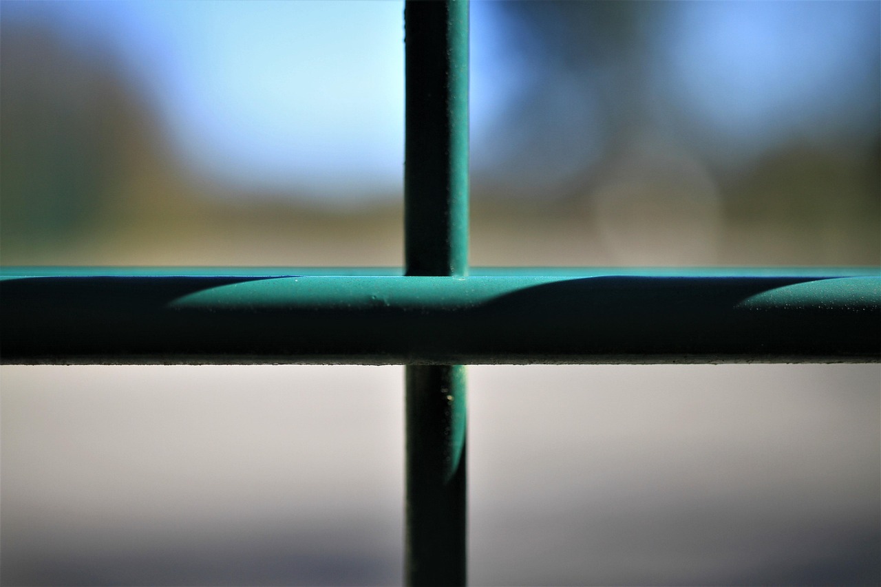 A locked metal gate across a green fenced corridor.